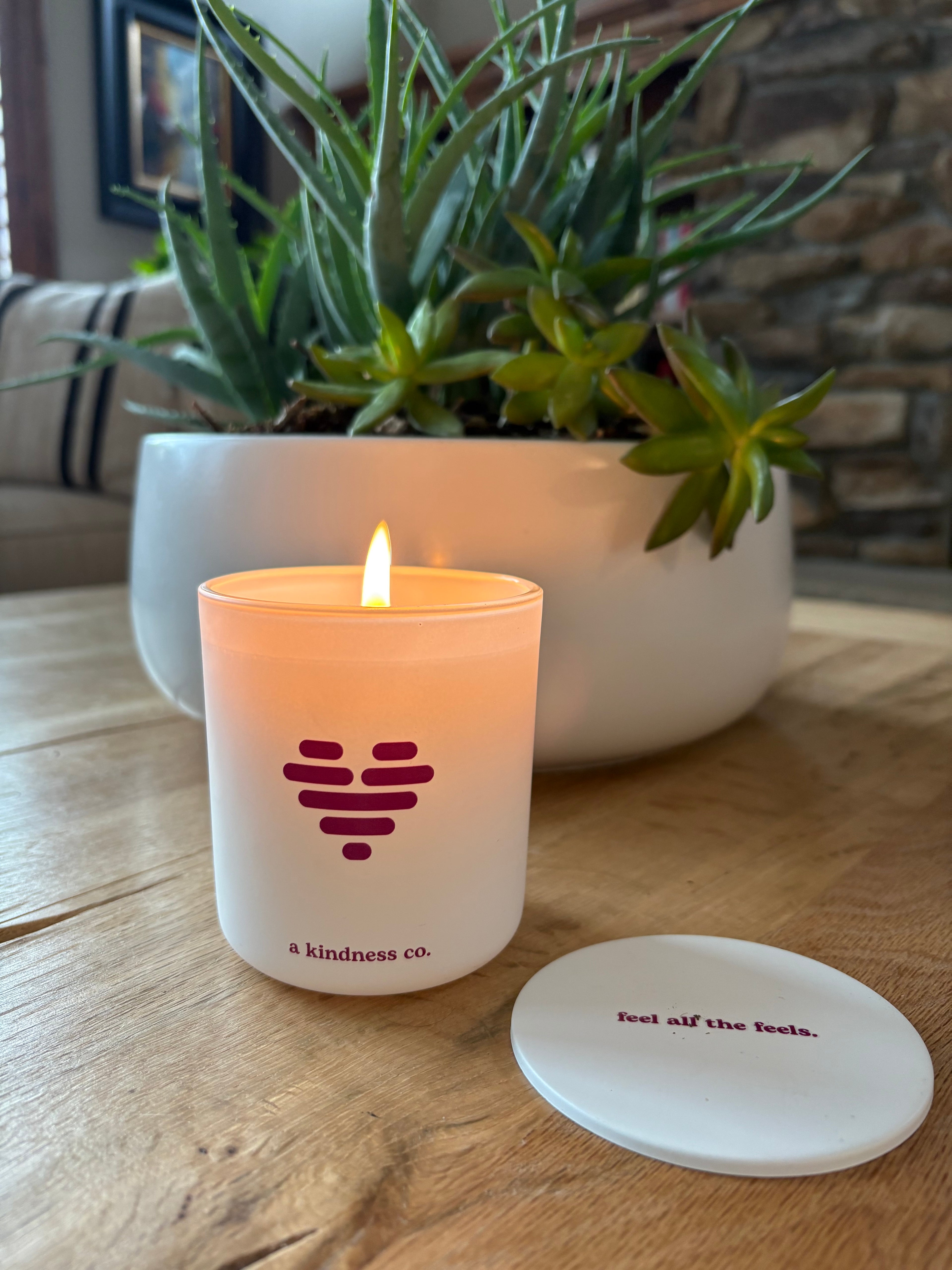 Luv scented soy candle with a heart logo on a wooden surface next to a plant and lid with feel all the feels message